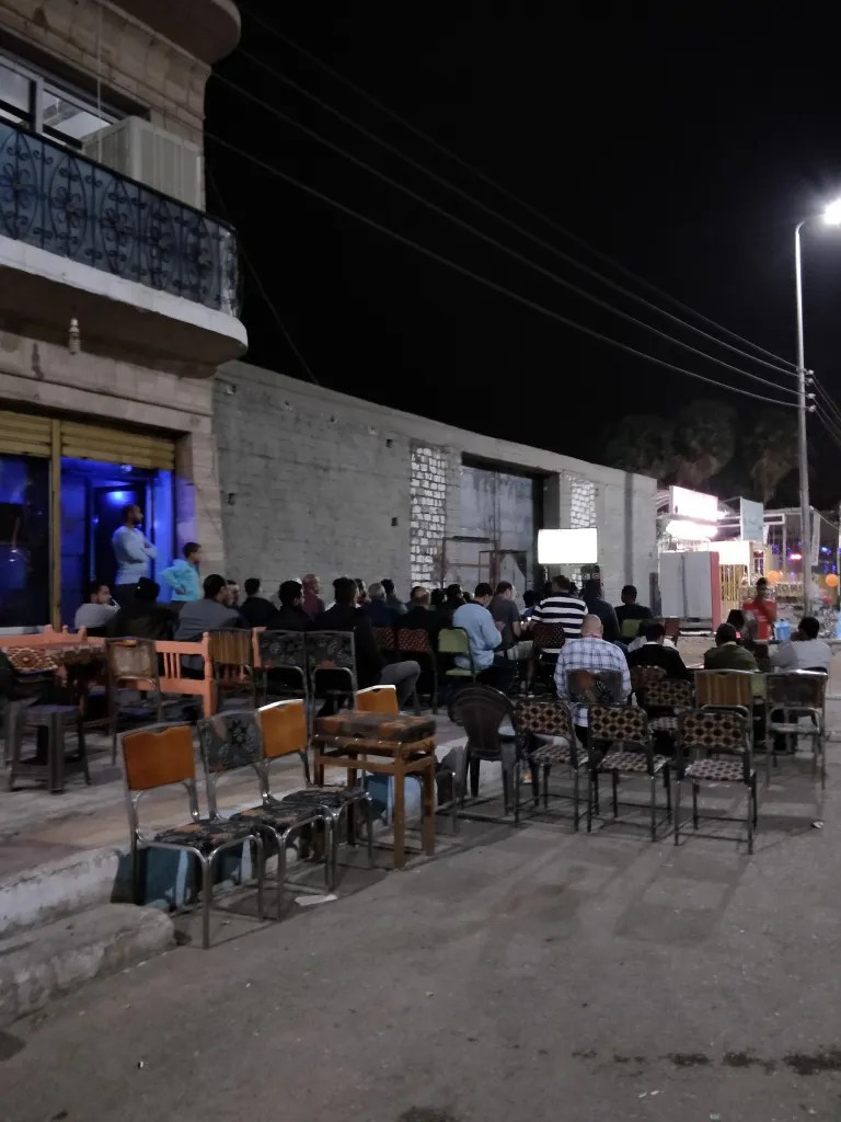 People sitting on the street watching football on a TV screen which enjoying shisha in the evening